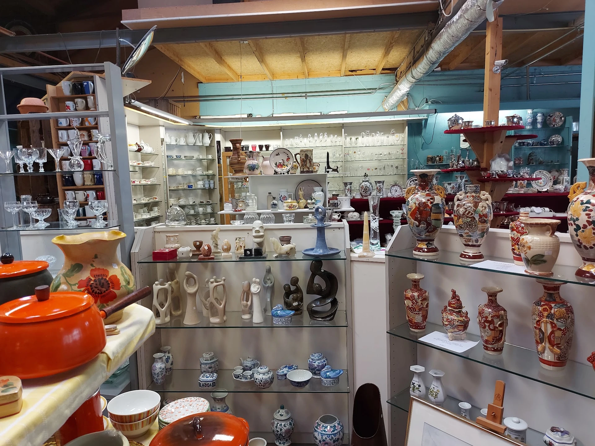 Glazen vitrines met uitgestalde serviesgoed, vazen, beeldjes en decoratieve artikelen in de kringloopwinkel
