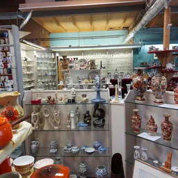 Glazen vitrines met uitgestalde serviesgoed, vazen, beeldjes en decoratieve artikelen in de kringloopwinkel