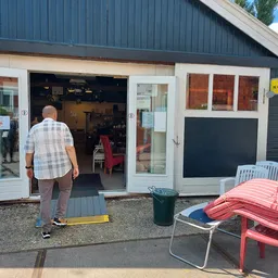 Voorgevel van kringloopwinkel met open deuren, terras met stoelen en tuinmeubilair ervoor