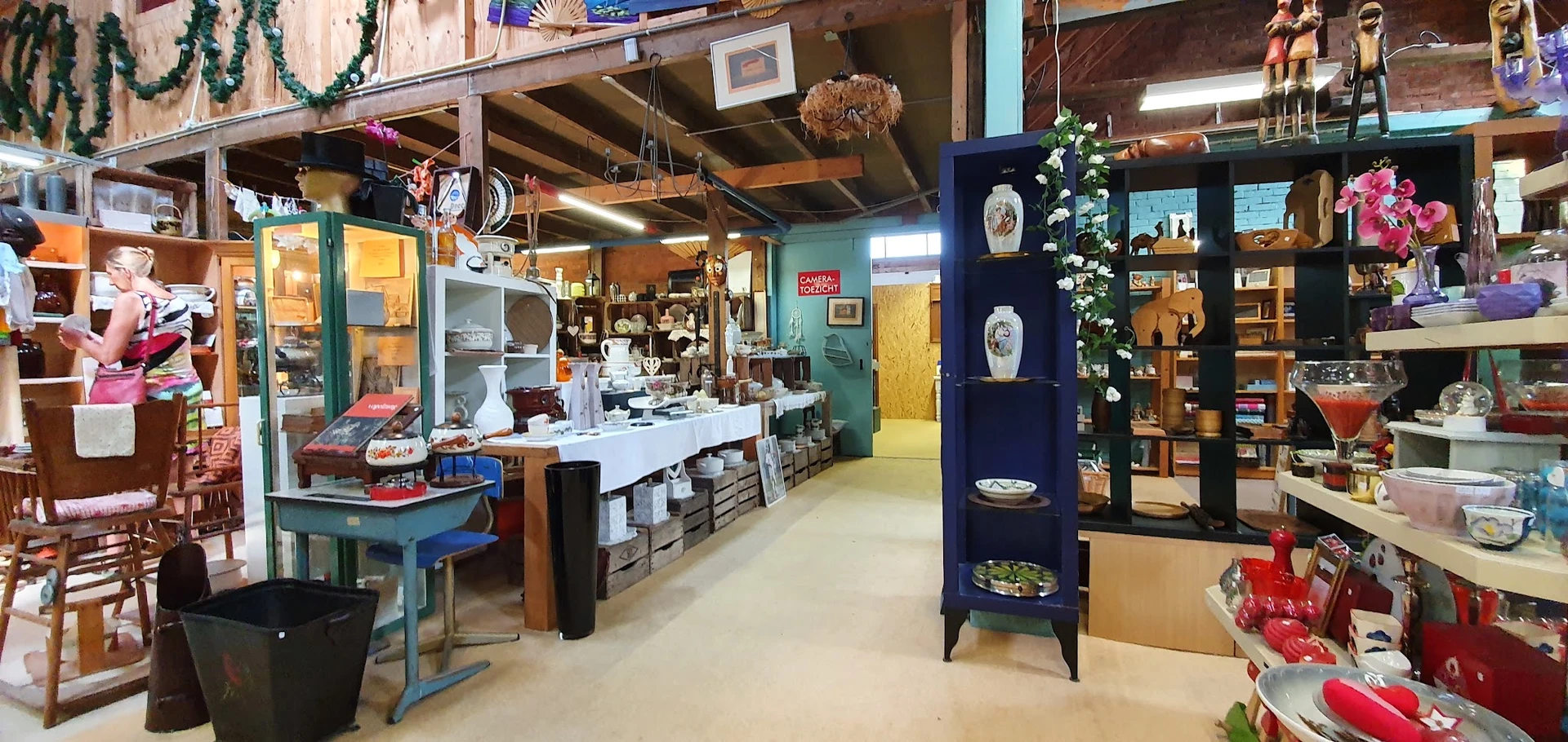 Winkelvloer van kringloopwinkel met toonbank, stellingen, diverse spullen en houten balkenplafond
