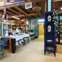 Winkelvloer van kringloopwinkel met toonbank, stellingen, diverse spullen en houten balkenplafond