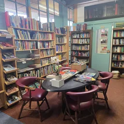 Leeshoek in kringloopwinkel met boekenkast, vier paarse fauteuils rond zwarte tafel en natuurlijk licht