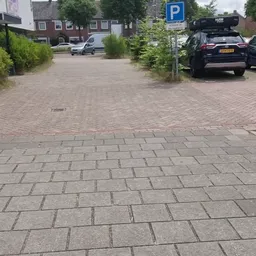 Parkeerplaats met tegels en auto's, winkelgebouw op achtergrond