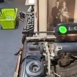 Close-up van een vintage typemachine met groene indicator, naast een gele krat en andere kantoorgerei