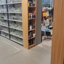 Winkelinterieur met glazen vitrinekast links en houten schappen in het midden, zicht op achterkamer met kinderwagen en stelli