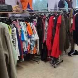 Rekken met tweedehands kleding in verschillende kleuren, waaronder rode, zwarte en gestreepte kledingstukken