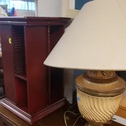 Twee lampen: een donkerrode houten tafel met louvredetails en een lamp met crème kleurige kap en goud-kleurige voet