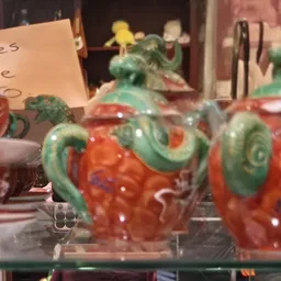 Twee rode decoratieve potjes met groene deksel en handvaten, uitgestald op een plank in de winkel