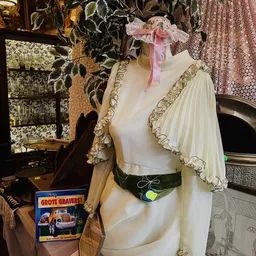 Crèmekleurige vintage jurk op etalagepop met geplooid mouwtje en groene ceintuur