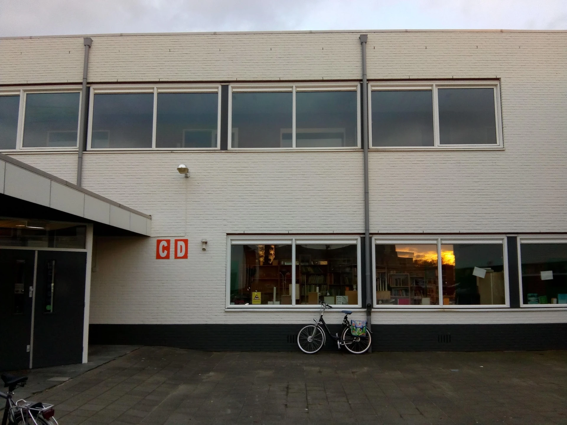 Voorgevel van kringloopwinkel met witte bakstenen muur, grote ramen en rode letters 'GD' op de deur