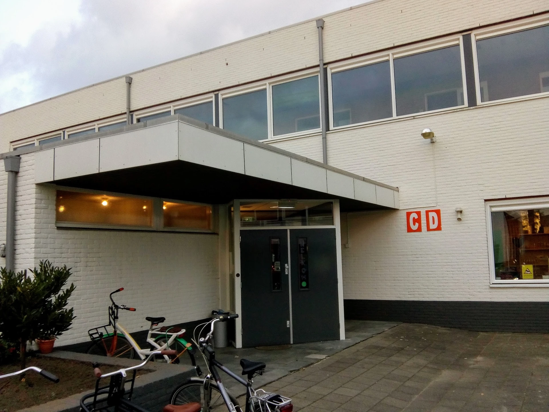 Witte gevel van kringloopwinkel met zwart afdak, glazen deuren en ramen, fietsen geparkeerd ervoor