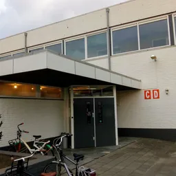 Witte gevel van kringloopwinkel met zwart afdak, glazen deuren en ramen, fietsen geparkeerd ervoor