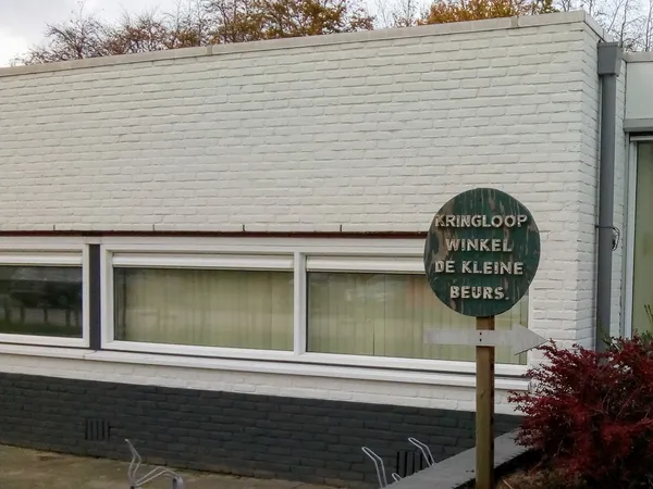 Witte gevel van kringloopwinkel met grote ramen en groen uithangbord met winkelnaam