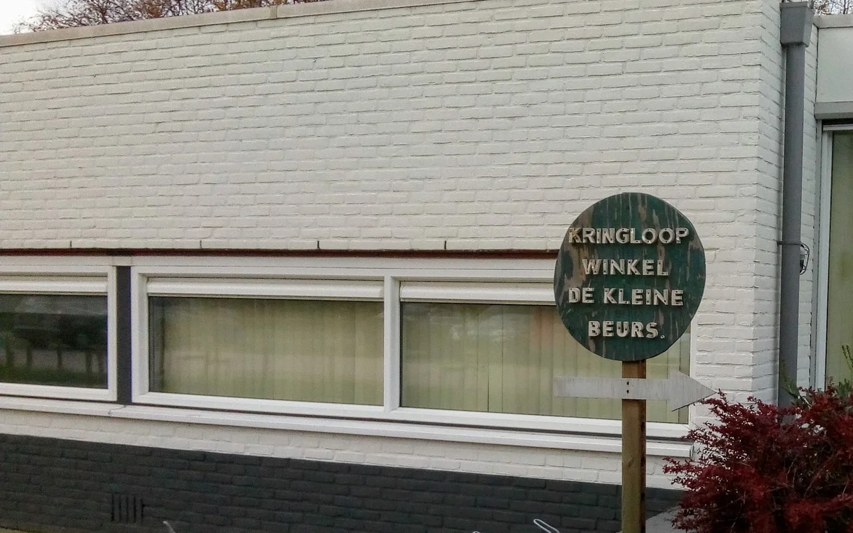 Witte gevel van kringloopwinkel met grote ramen en groen uithangbord met winkelnaam