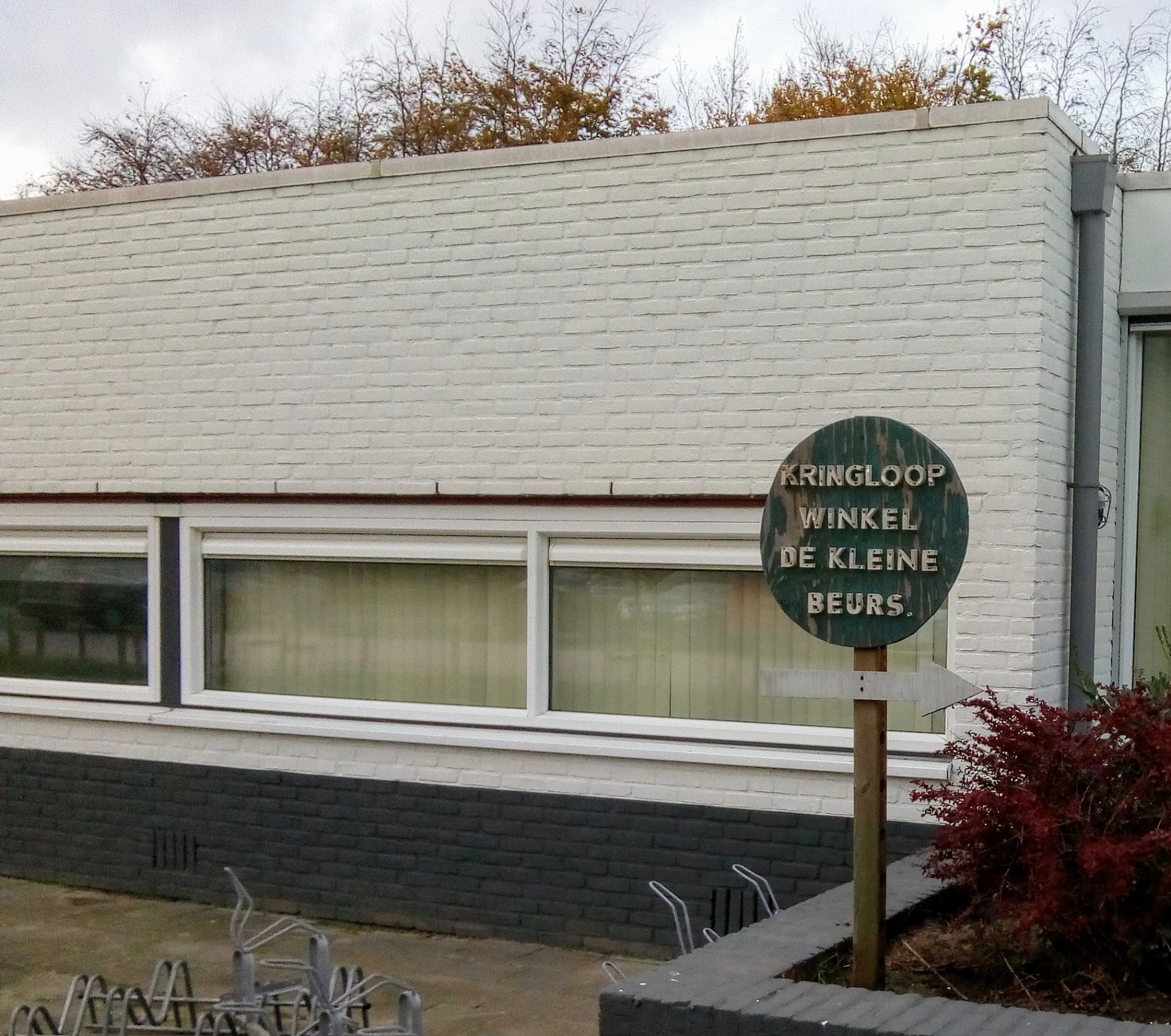 Witte gevel van kringloopwinkel met grote ramen en groen uithangbord met winkelnaam