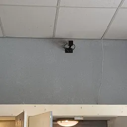 Muurdetail met zwarte beugel en witte kabel tegen grijze achtergrond