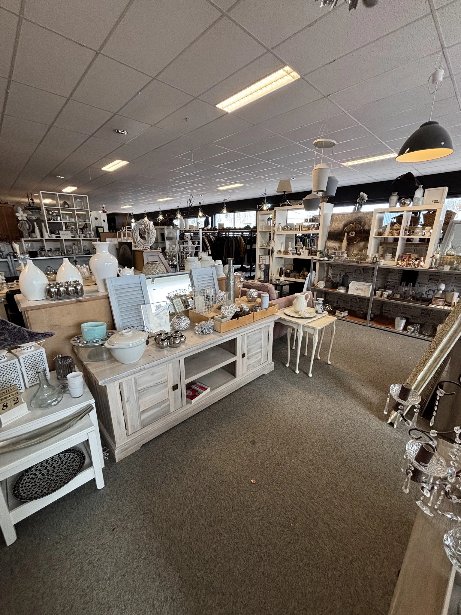 Overzicht van de winkelruimte met verschillende vitrines, een houten toonbank en diverse huishoudartikelen en decoratie.