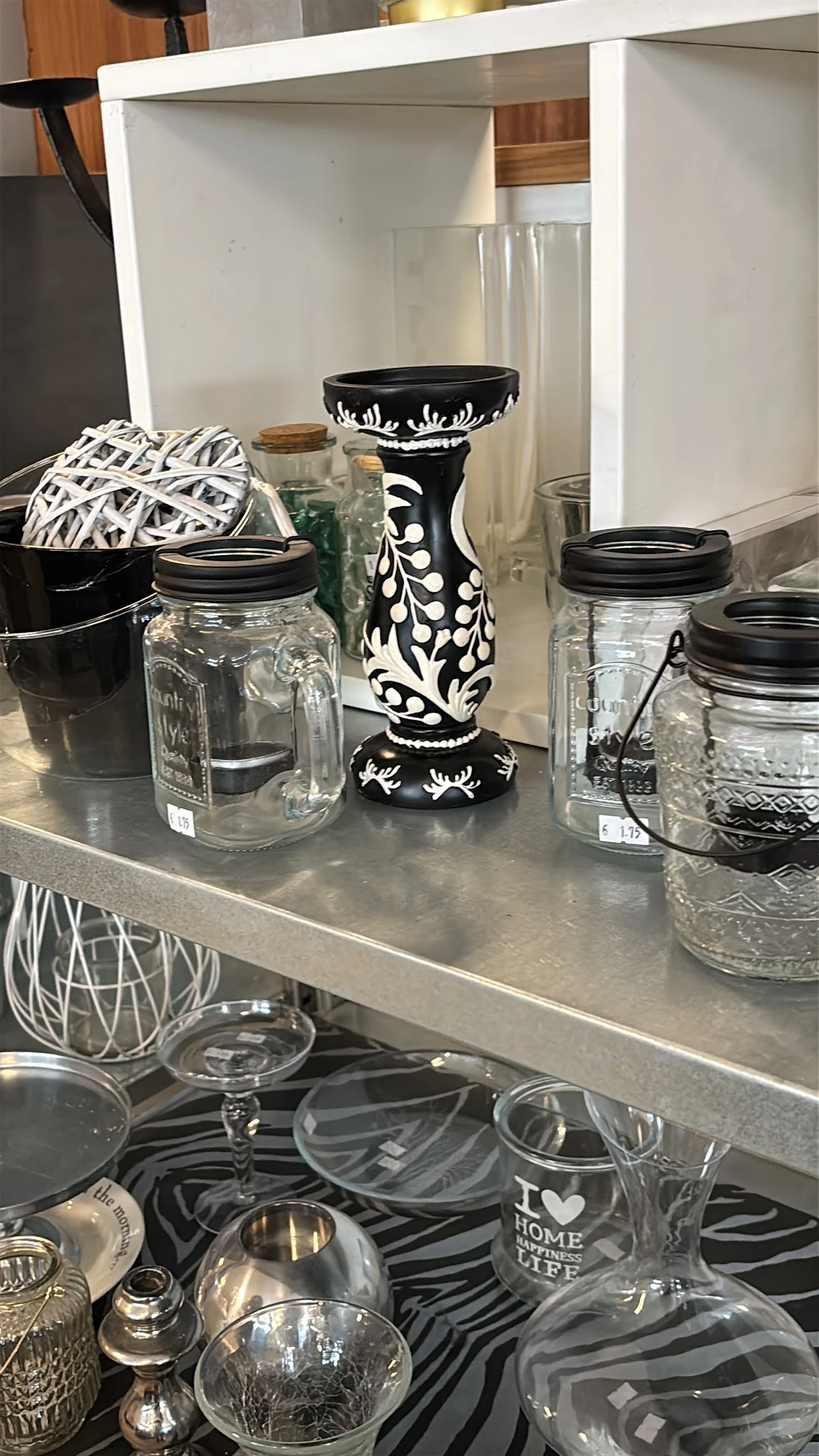 Glazen potten met zwarte deksels en decoratieve items op een grijze plank in de winkel