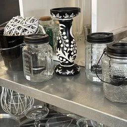 Glazen potten met zwarte deksels en decoratieve items op een grijze plank in de winkel