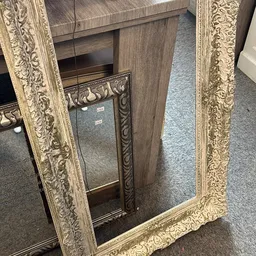 Twee sierlijk ingelijste spiegels met goudkleurige ornamentale lijsten naast elkaar.
