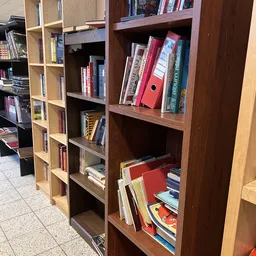 Houten boekenkasten met tweedehands boeken en een rode doos op diverse planken