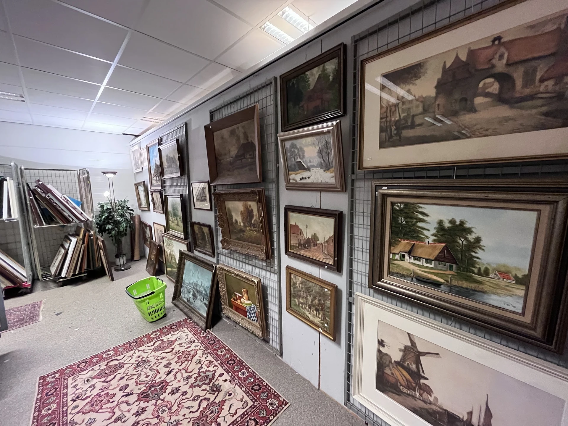 Uitgestalde schilderijen en prenten in houten lijsten op stellingen in de winkel