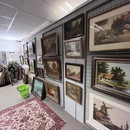 Uitgestalde schilderijen en prenten in houten lijsten op stellingen in de winkel