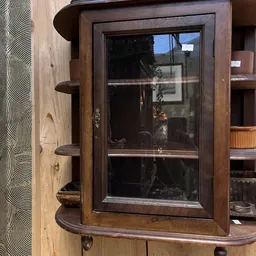 Houten vitrinekast met glazen deuren en houten planken tegen bruine wand