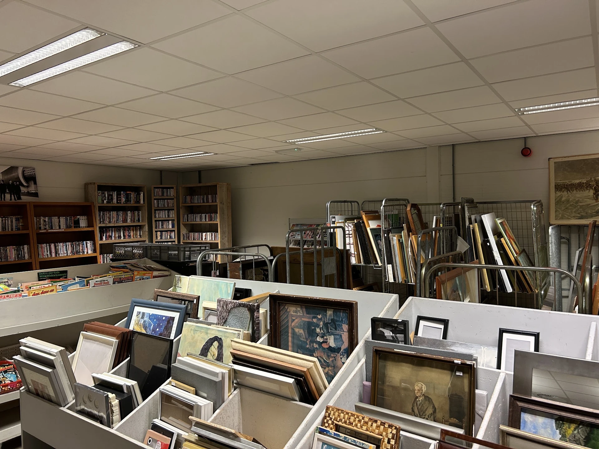 Winkelbinnenruimte met boekenkasten, stellingen met ingelijste schilderijen, kunstwerken en diverse gebruiksvoorwerpen