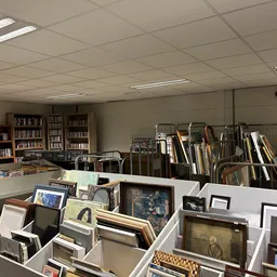 Winkelbinnenruimte met boekenkasten, stellingen met ingelijste schilderijen, kunstwerken en diverse gebruiksvoorwerpen