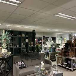 Winkelvloer met stellingen vol huisraad, decoratieartikelen en een grijze bank als display in kringloopwinkel