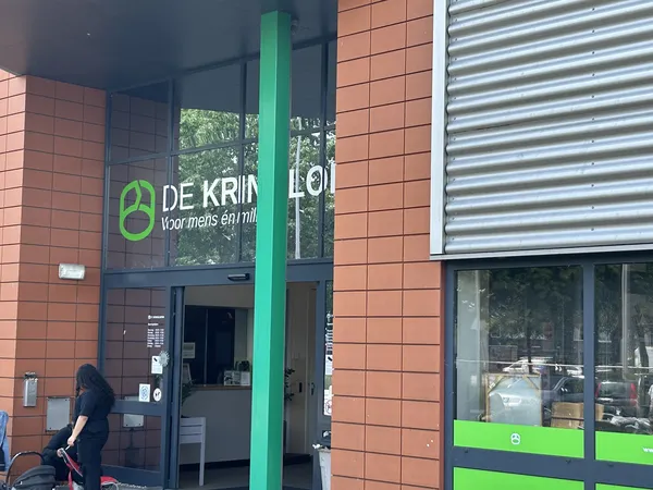Ingang van kringloopwinkel met groene pijler, rode bakstenen gevel en groene accenten