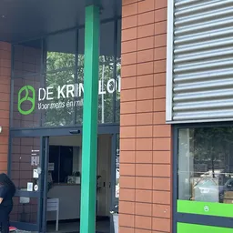 Ingang van kringloopwinkel met groene pijler, rode bakstenen gevel en groene accenten