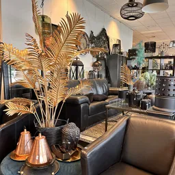 Sfeervolle winkelruimte met zwarte leunstoel, gouden decoratieve palmtakken, boekenkasten en diverse huisraadartikelen