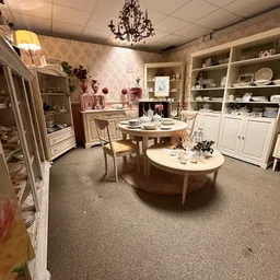 Winkelinterieur met witte kasten, twee ronde tafels met servies, roze wandafwerking en decoratieve items.