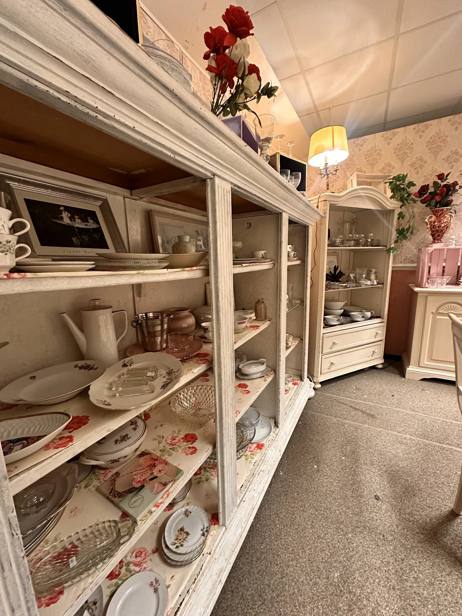 Witte kasten met glasdeuren vol serviesgoed, borden en decoratieve voorwerpen in een kringloopwinkel