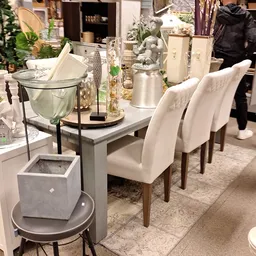 Grijze eettafel met witte stoelen en decoratieve accessoires in een interieurshow