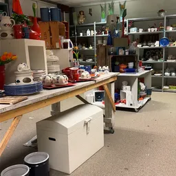 Winkelvloer met tafel vol huishoudartikelen, servies en decoratie, stellingen op achtergrond