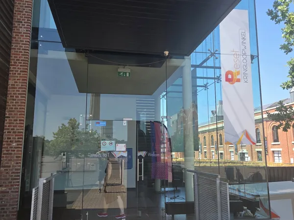 Glazen ingang van kringloopwinkel met moderne luifel, uitzicht op winkelstraat met historische gebouwen