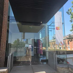 Glazen ingang van kringloopwinkel met moderne luifel, uitzicht op winkelstraat met historische gebouwen