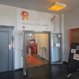 Winkelentree met glazen deuren, lift aan de linkerkant en duidelijk zichtbare Reset Kringloopwinkel signage boven de ingang
