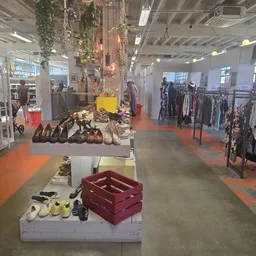 Grote winkelvloer met oranje vloerstroken, diverse rekken met kleding en schoenendisplays in een kringloopwinkel
