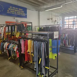 Rekken met tweedehands kleding in diverse kleuren, voornamelijk sportkleding en gele/neon items