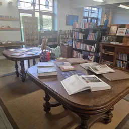 Bibliotheekruimte met houten tafels vol opengeslagen boeken, boekenkasten en boekenrekken