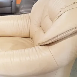 Close-up van een crèmekleurig lederen fauteuil met armleuningen en gestikte details