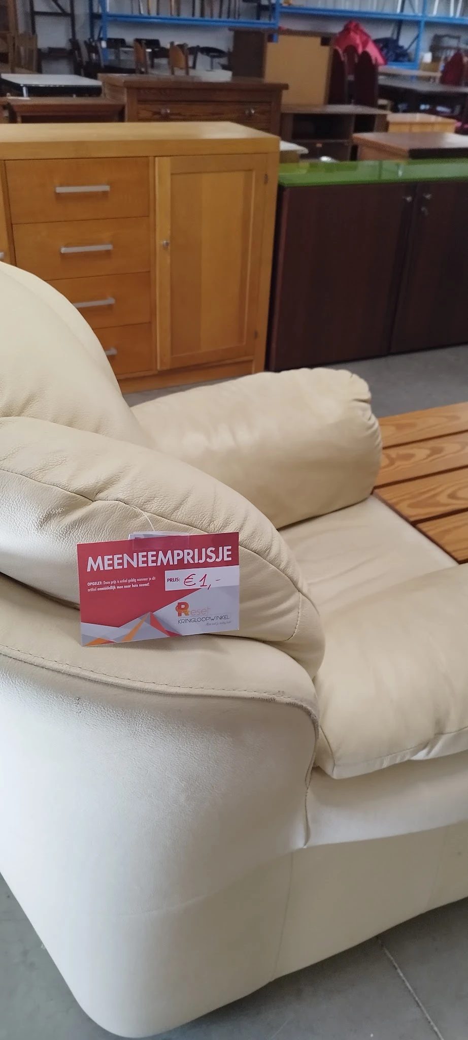 Close-up van een beige/crème kleurig kussen met een rood prijskaartje 'MEENEEMPRIJSJE' erop
