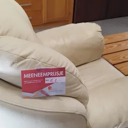 Close-up van een beige/crème kleurig kussen met een rood prijskaartje 'MEENEEMPRIJSJE' erop