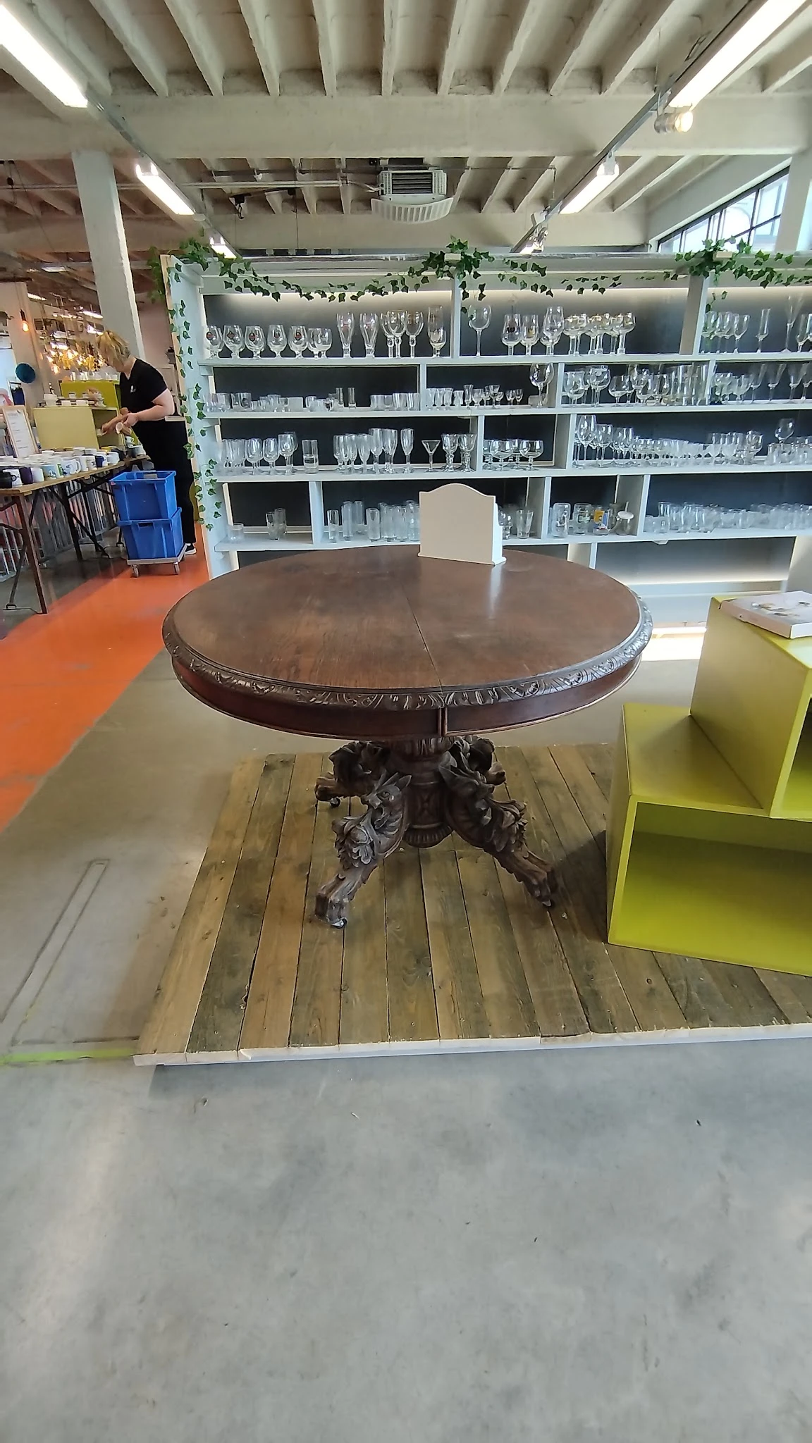 Ronde houten tafel met ornamentaal gesneden voet en decoratieve rand, staande in een kringloopwinkel