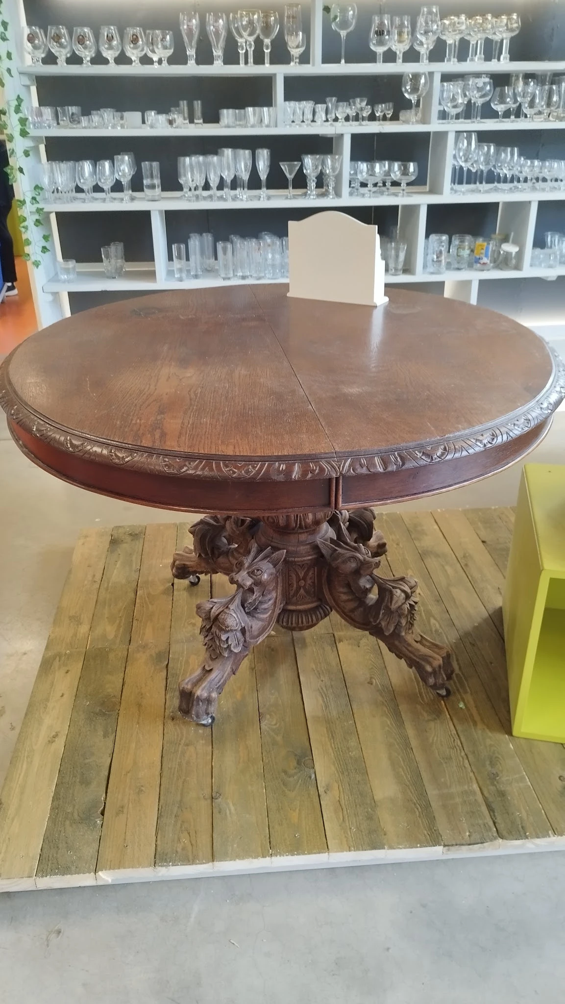 Ronde houten tafel met ornamentaal gesneden voet en decoratieve rand, geplaatst op gele vloerplanken