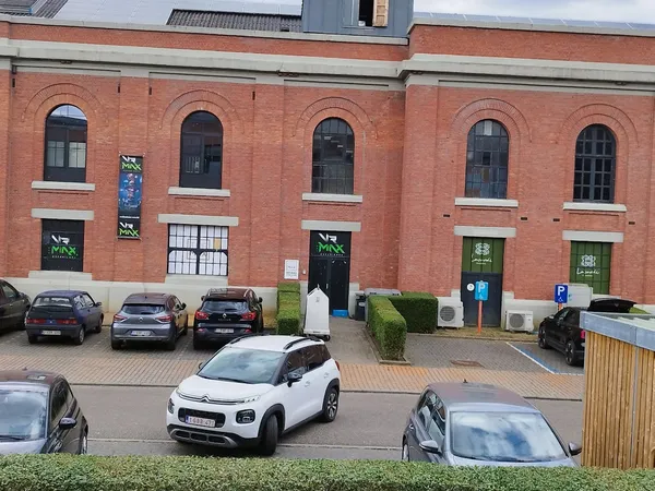 Bakstenen gevel van kringloopwinkel met groene deuren, parkeerplaats met auto's voor het pand